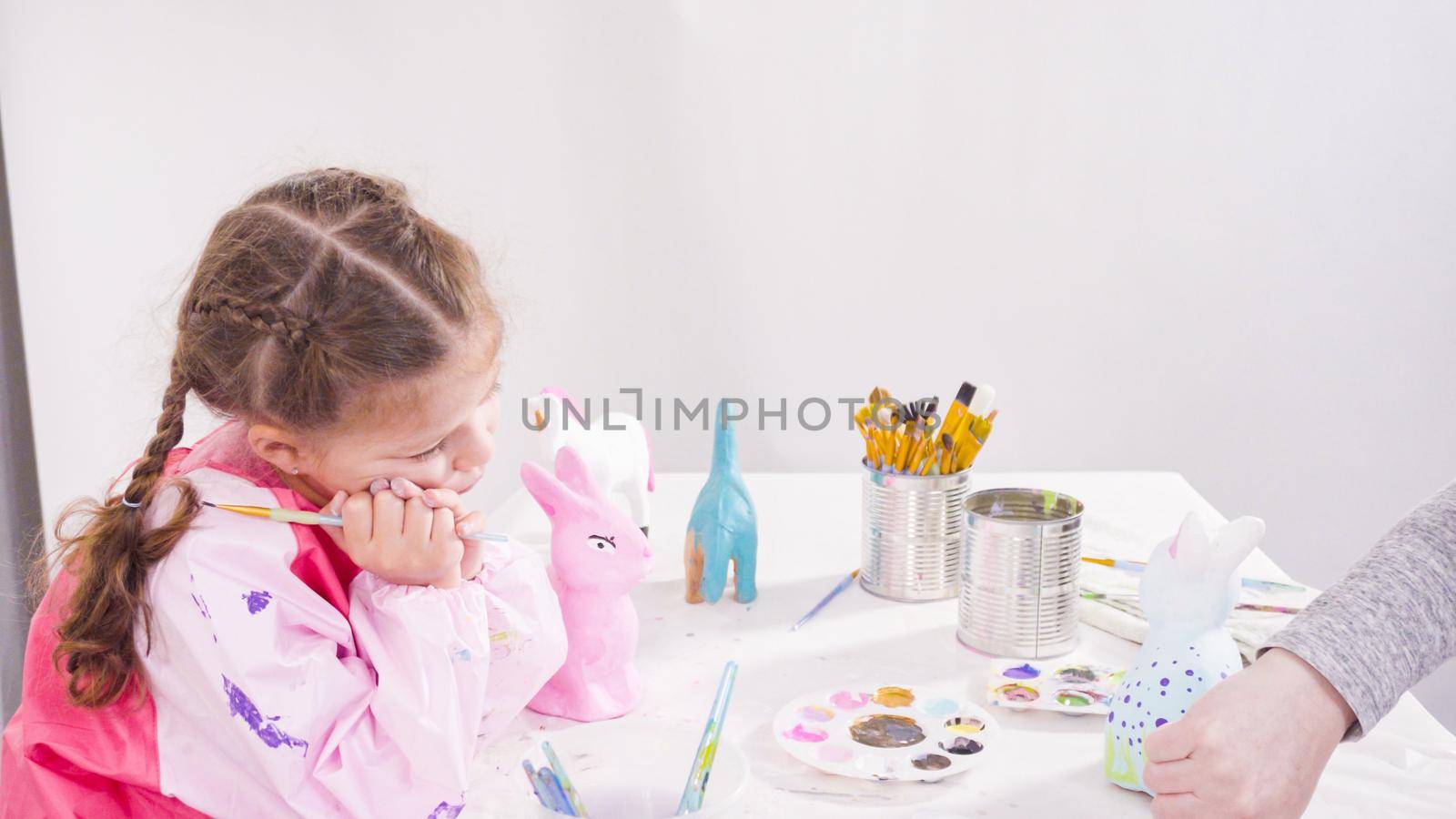 Little girl painting paper mache figurines with acrylic paint for her homeschooling art project.