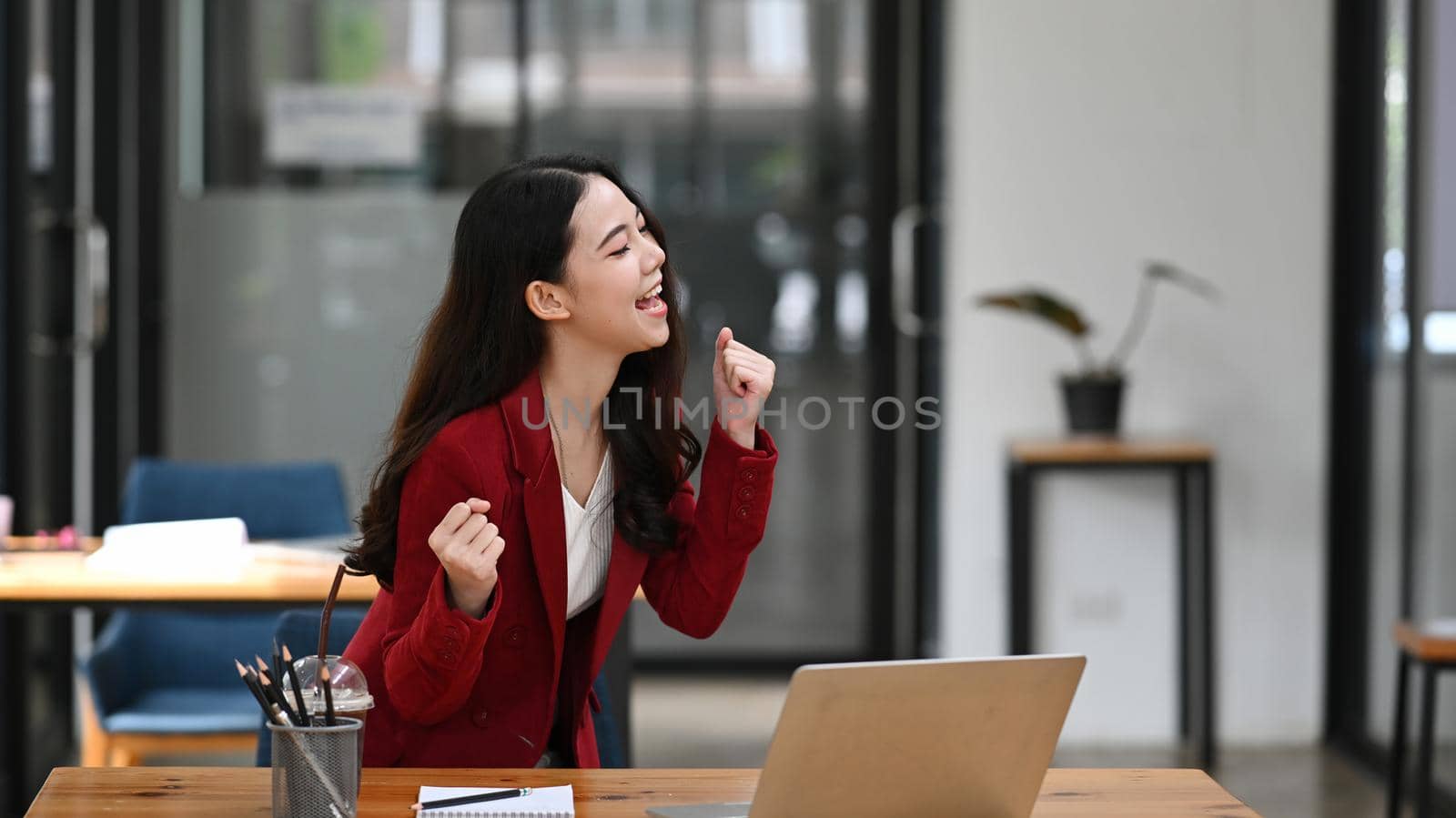 Excited businesswoman standing at her workplace and celebrating important achievement.