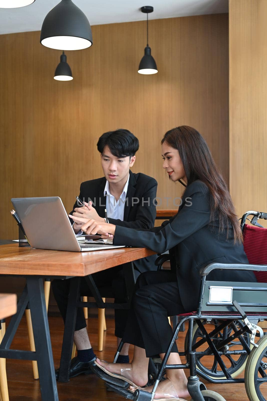 Smiling businesswoman in a wheelchair working in office with her colleague. by prathanchorruangsak