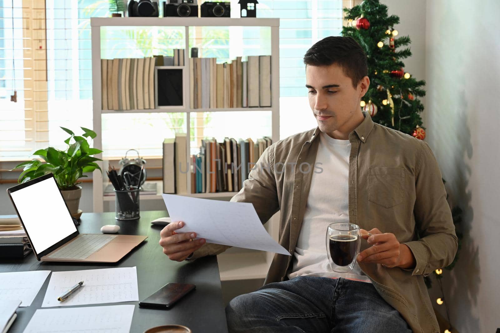 Young man holding coffee cup and reading some document.