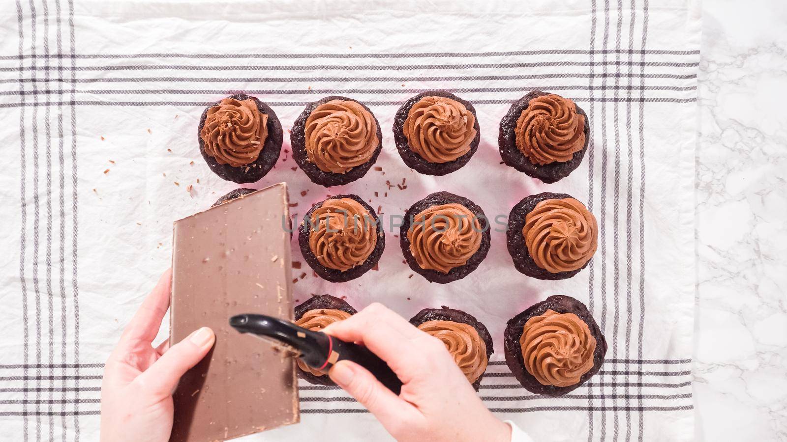 Flat lay. Step by step. Shaving chocolate bar on top of chocolate cupcakes frosted with chocolate ganache frosting.