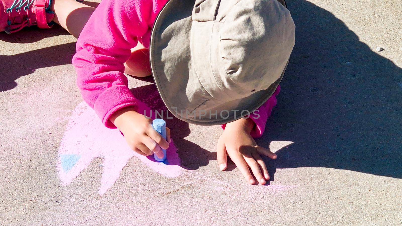 Little girl drawing with chalk on a sidewalk on the summer day.