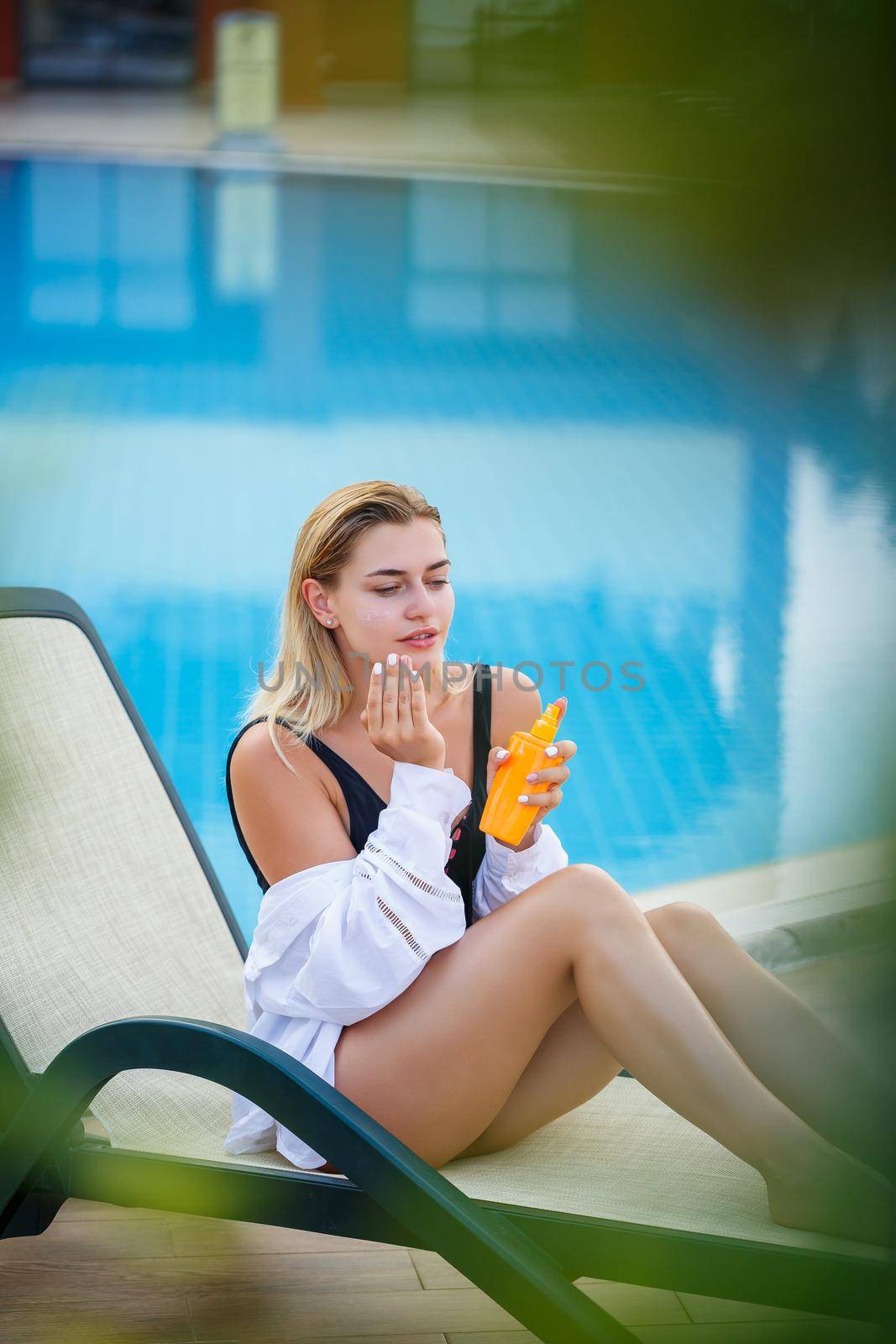 Attractive womav applying sunscreen on her face by the pool. Vacation sun protection factor