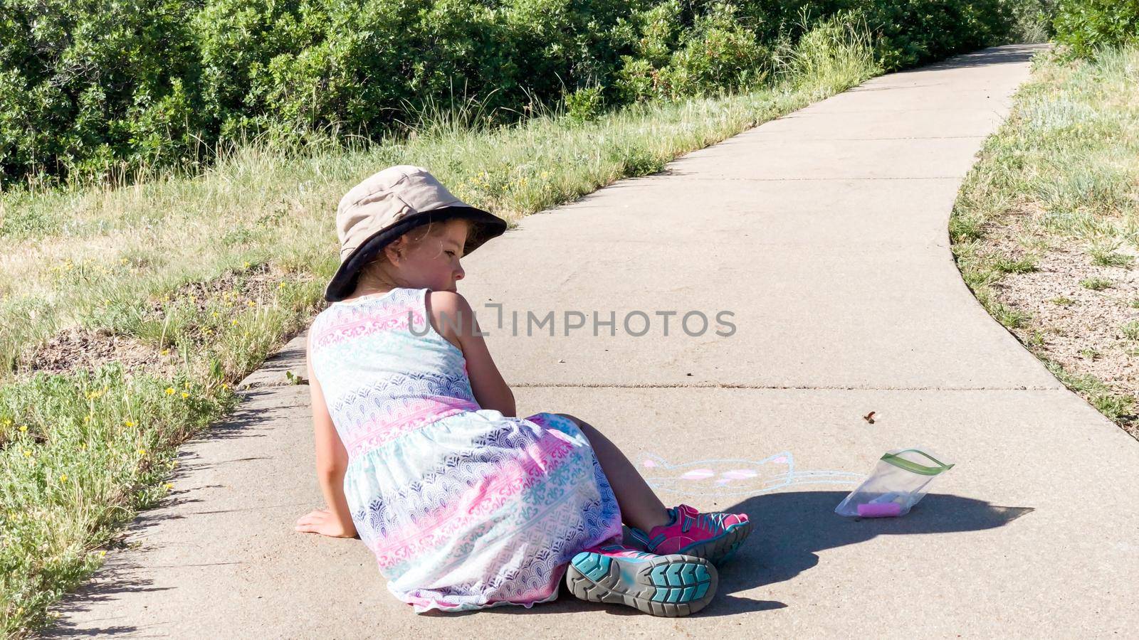 Little girl drawing with chalk on a sidewalk on the summer day.