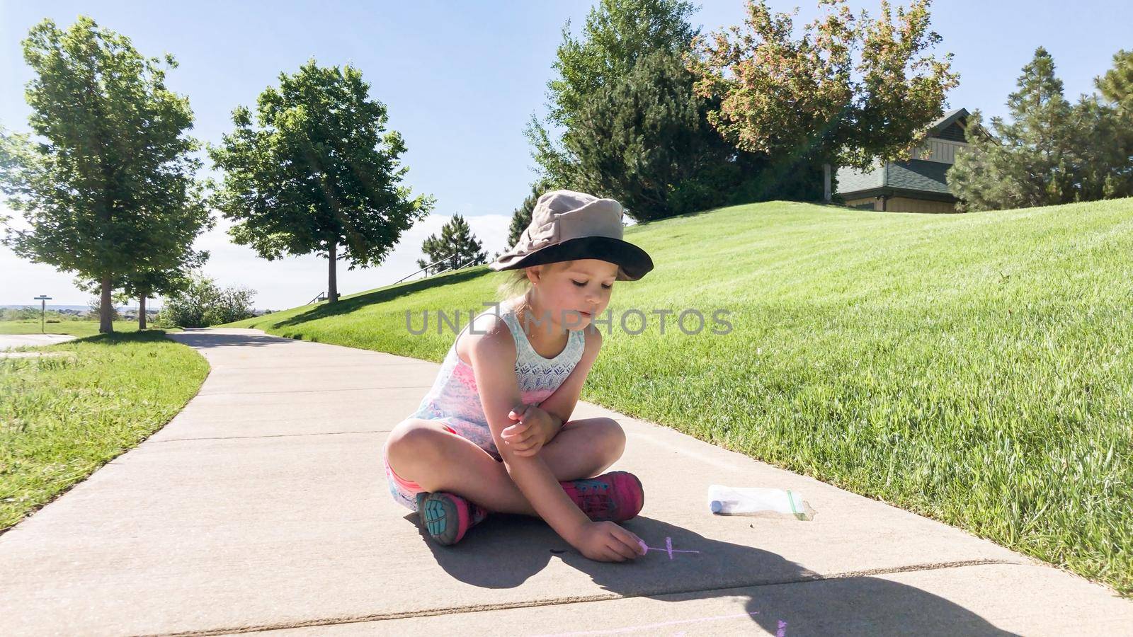 Little girl drawing with chalk on a sidewalk on the summer day.