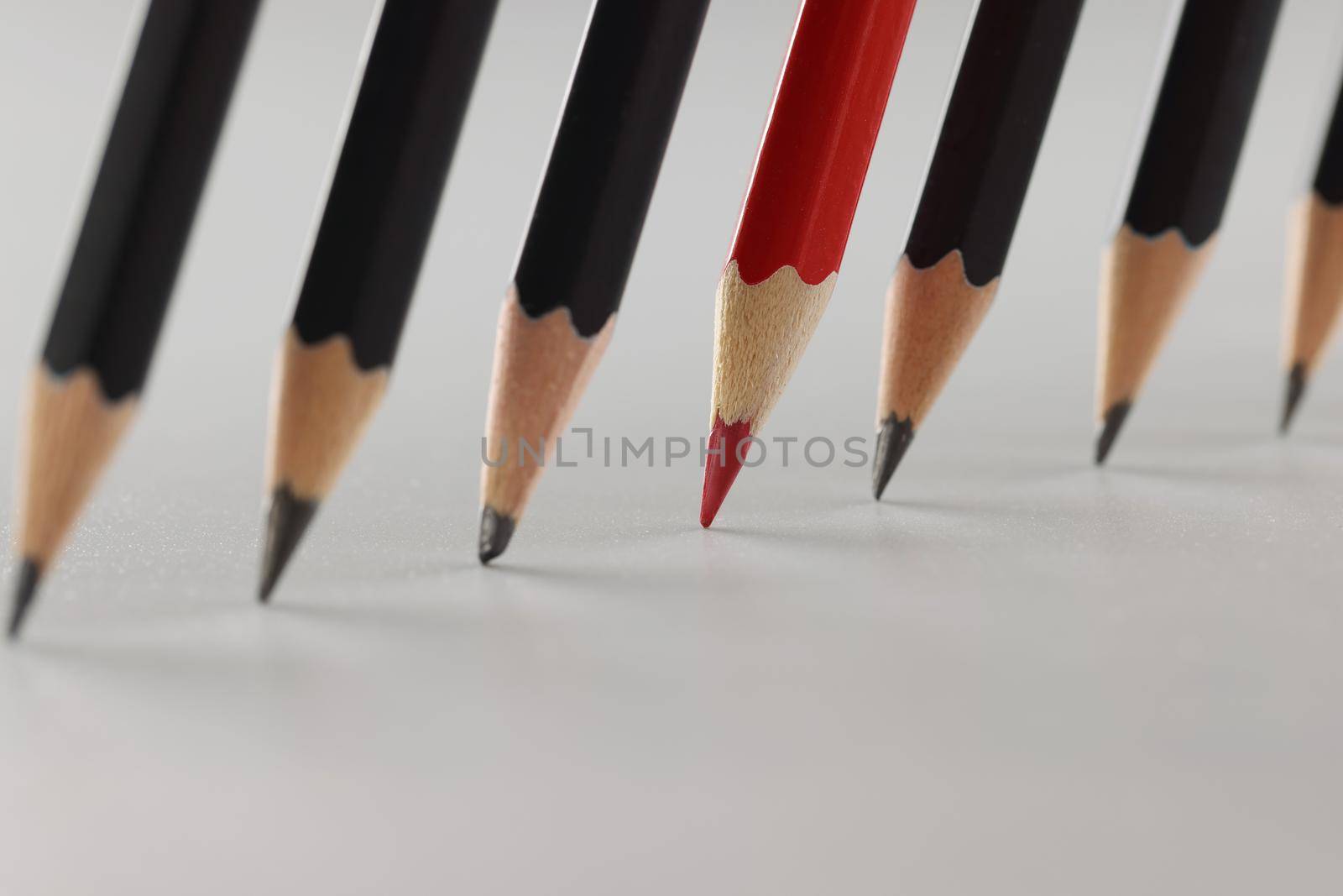 Red sharp slate pencil among black pencils in a row on a gray background. The concept of individuality, outstanding ability