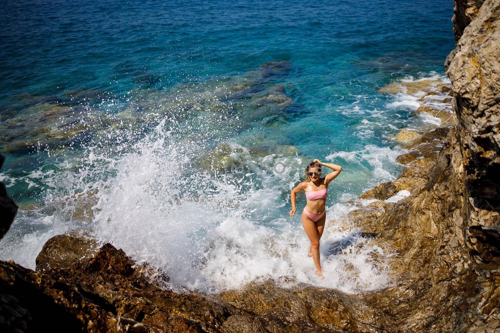 Young beautiful woman in a swimsuit stands on a rocky beach of the Mediterranean Sea. The concept of sea recreation. Selective focus