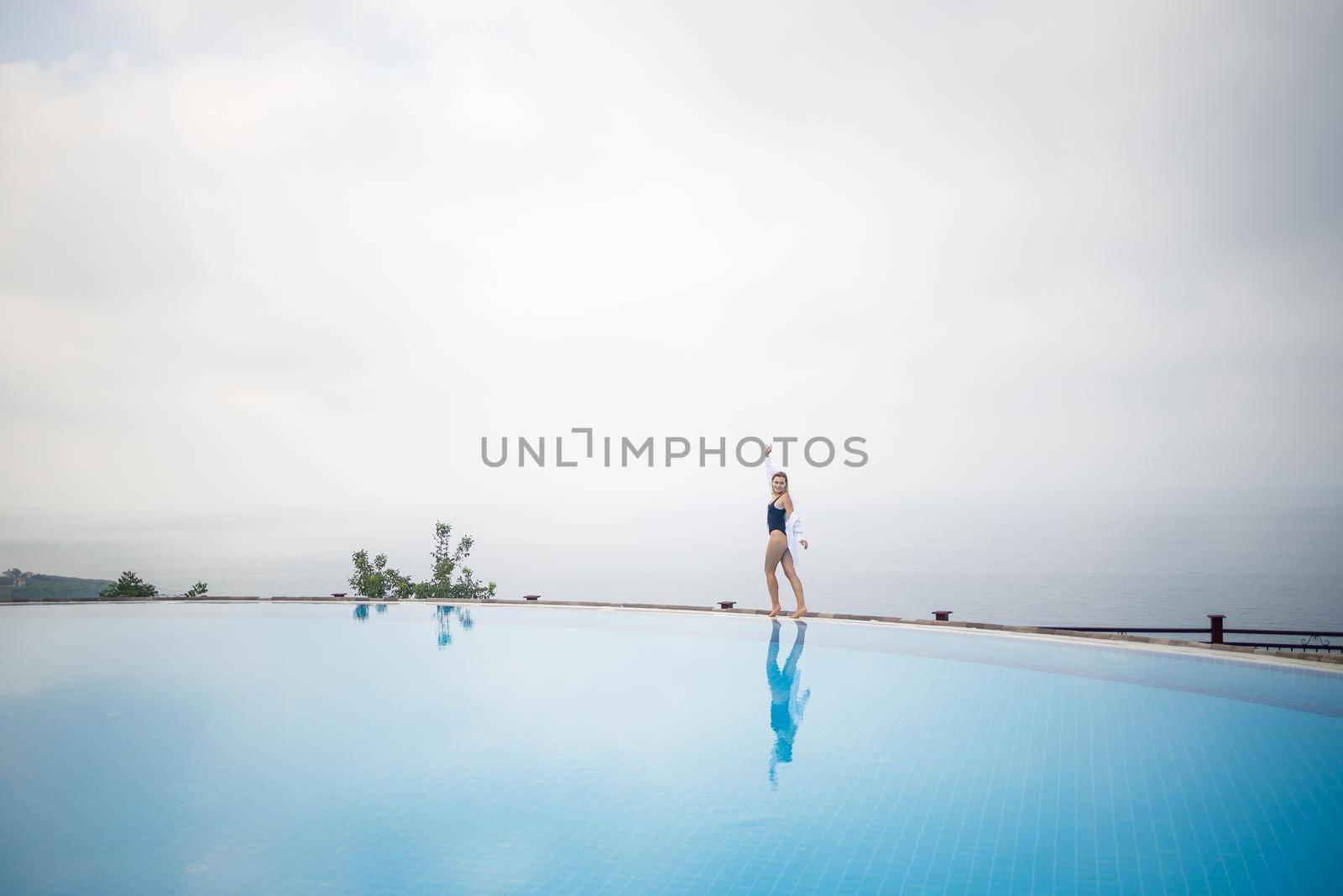 Beautiful woman in black swimsuit posing near outdoor pool with sea view by Dmitrytph