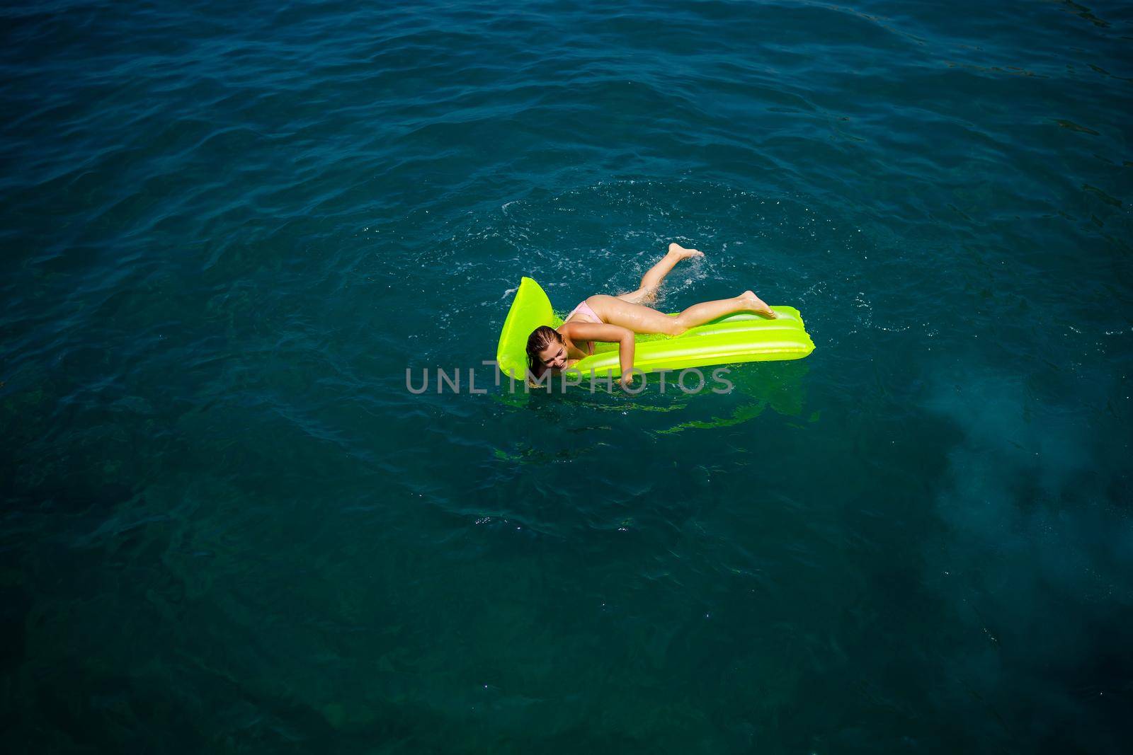 A young woman in a swimsuit swims on an inflatable bright mattress in the sea. Summer vacation concept.