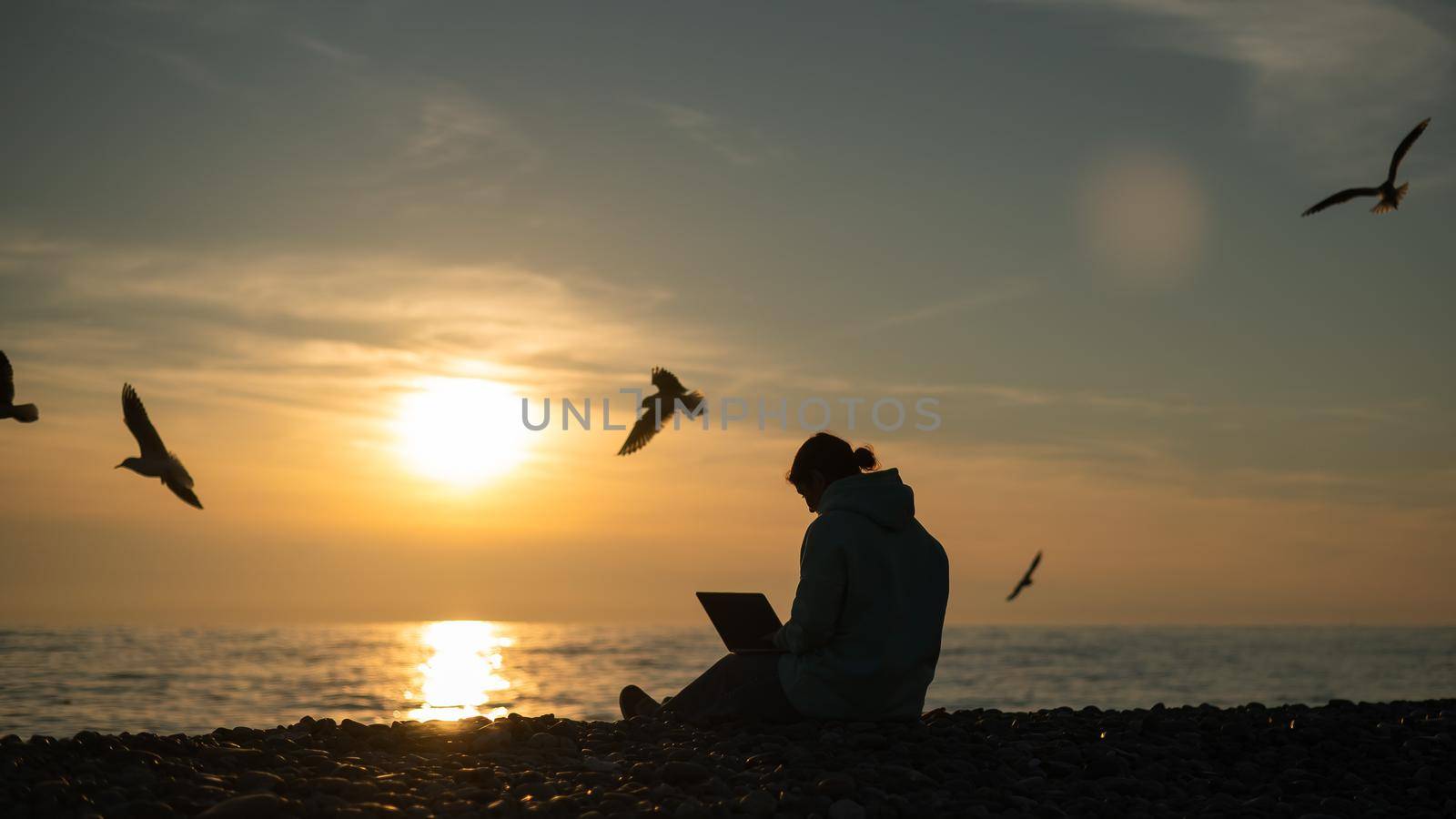 Caucasian woman typing on a laptop on the seashore at sunset. Freelance work. by mrwed54