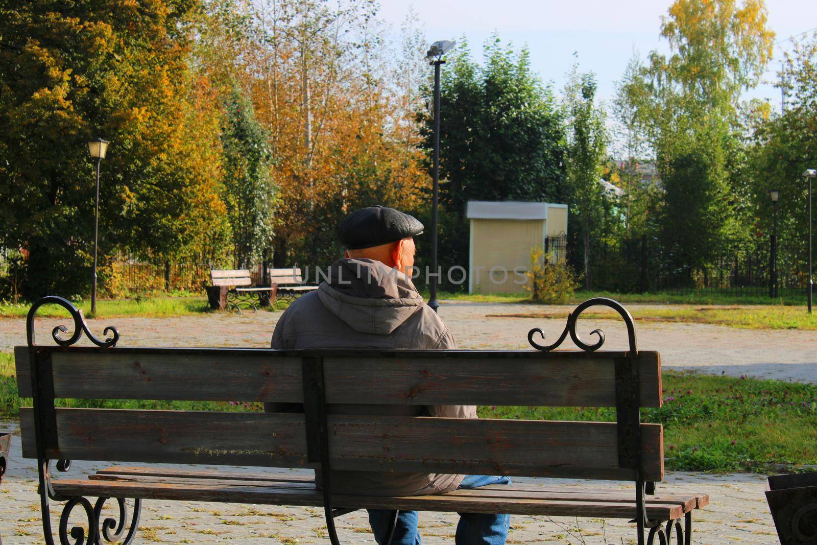 An elderly man sits on a bench in a city park.. by IronG96