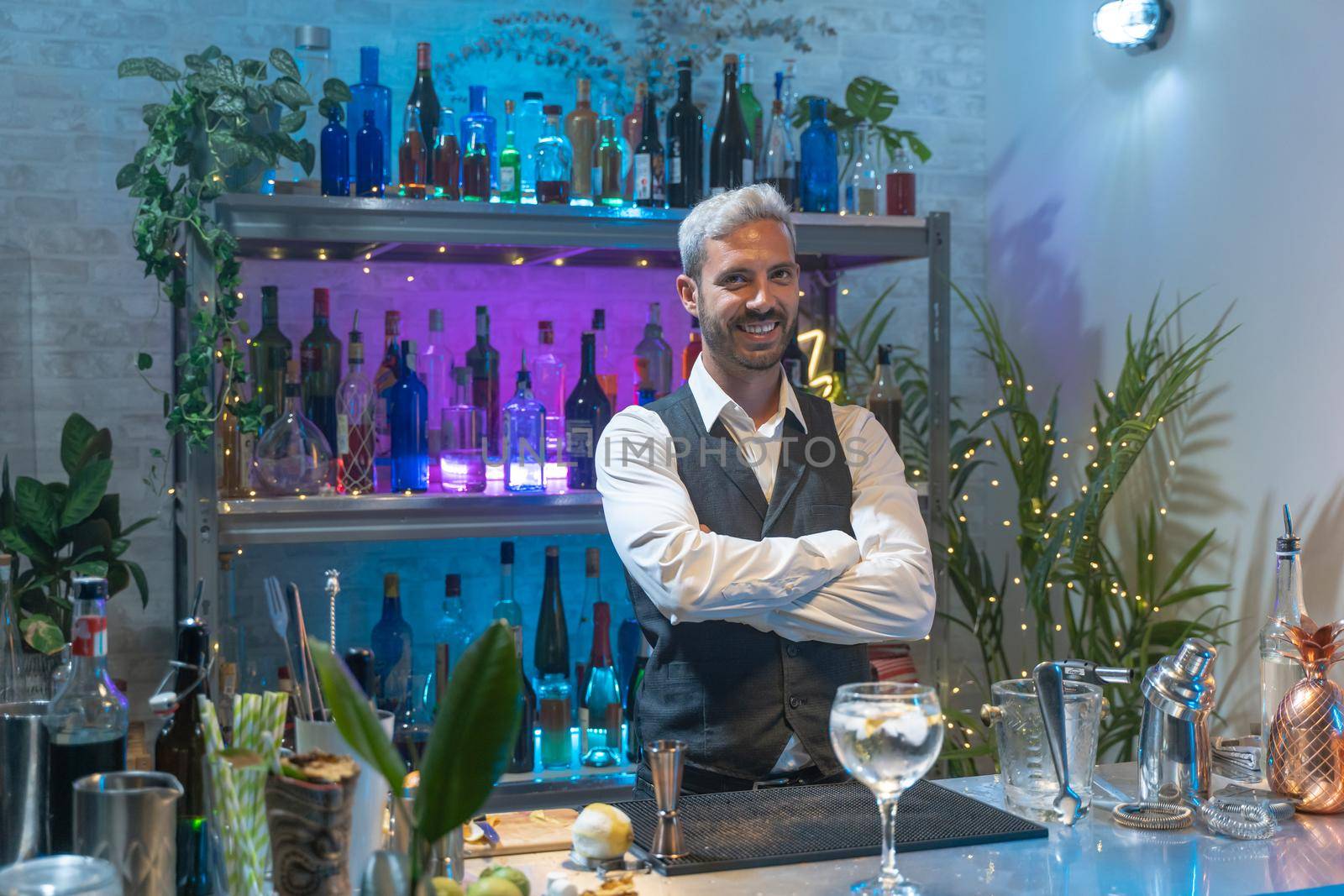 Barman portrait in a white shirt and black apron smiling looking to camera at party in nightclub. Night life. High quality photo