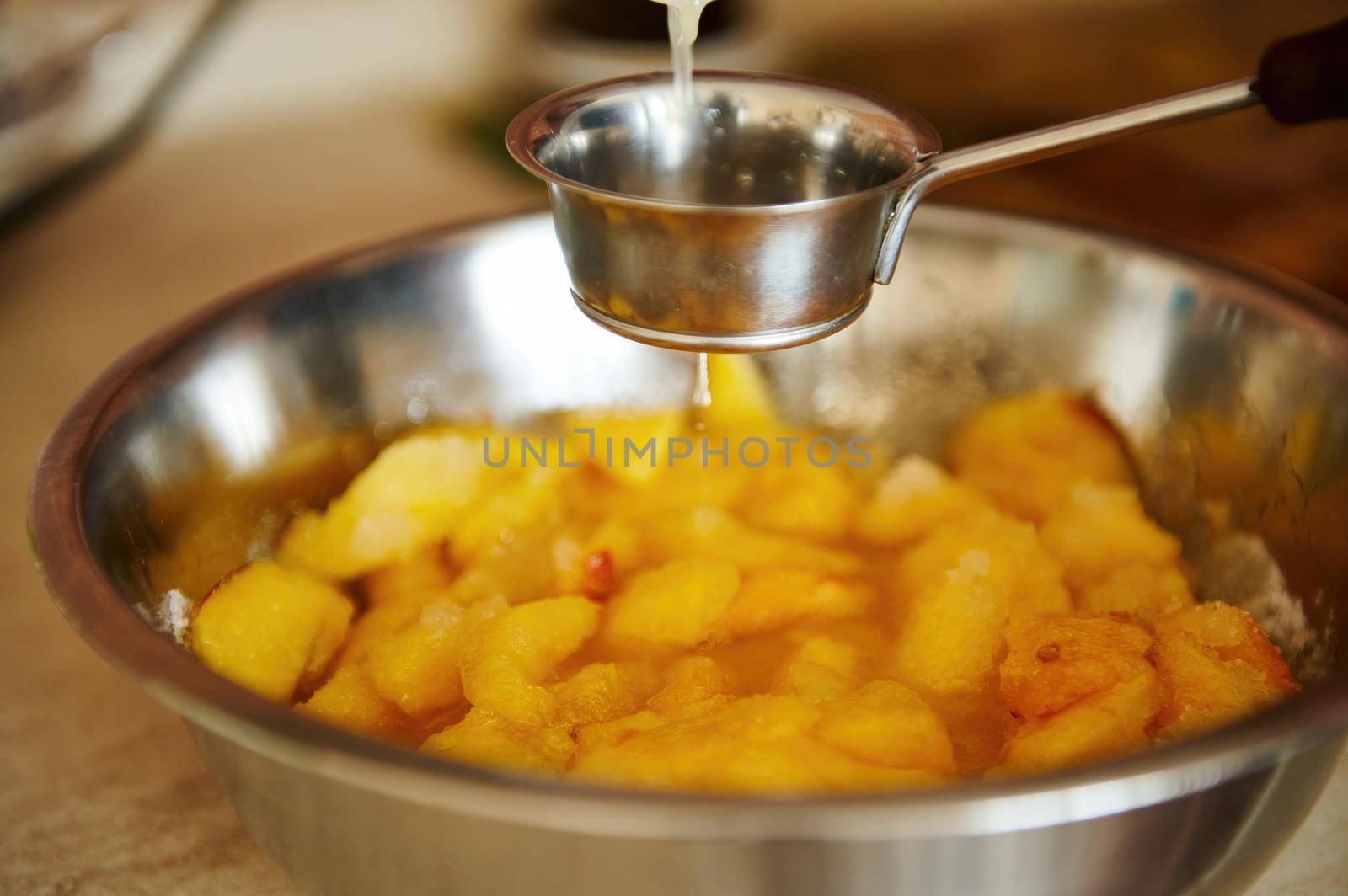 Pouring lemon juice into a metal bowl with sliced peaches while preparing homemade peach confiture or jam. Canning food by artgf