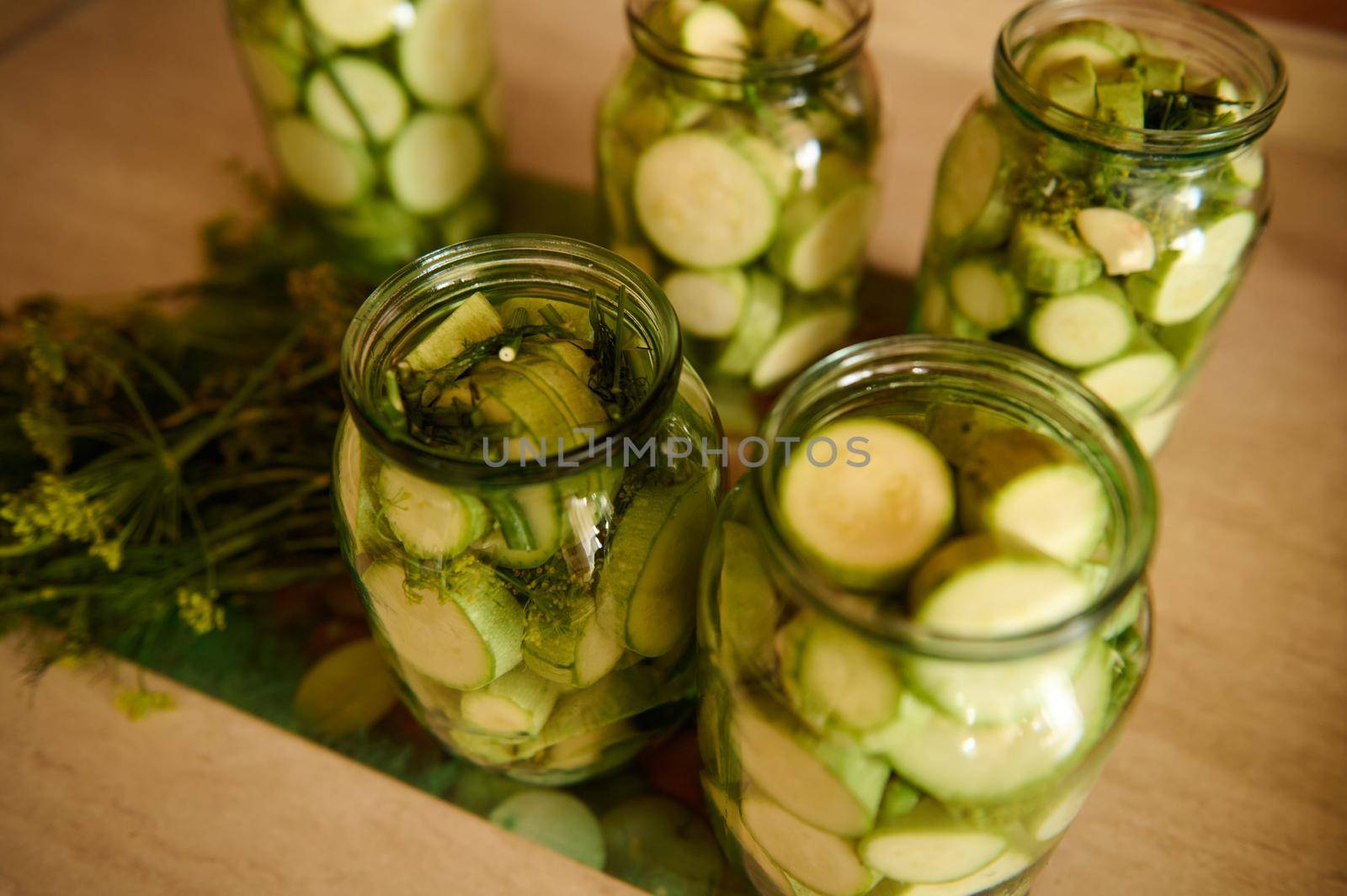 Top view of sterilized glass jars with pickled slices of ripe organic courgettes marinated in vinegar pickle, with fresh dill, garlic cloves. Food preservation. Canning. Preserving for the winter