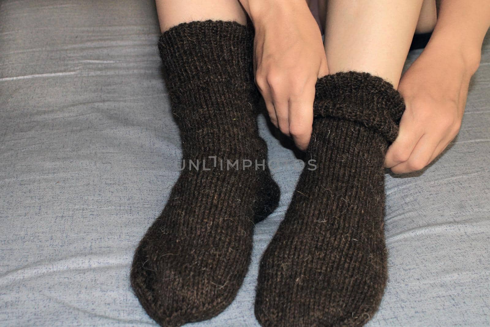 A young woman with slender legs sits on the bed at home and puts on woolen socks. The concept of the world energy crisis.
