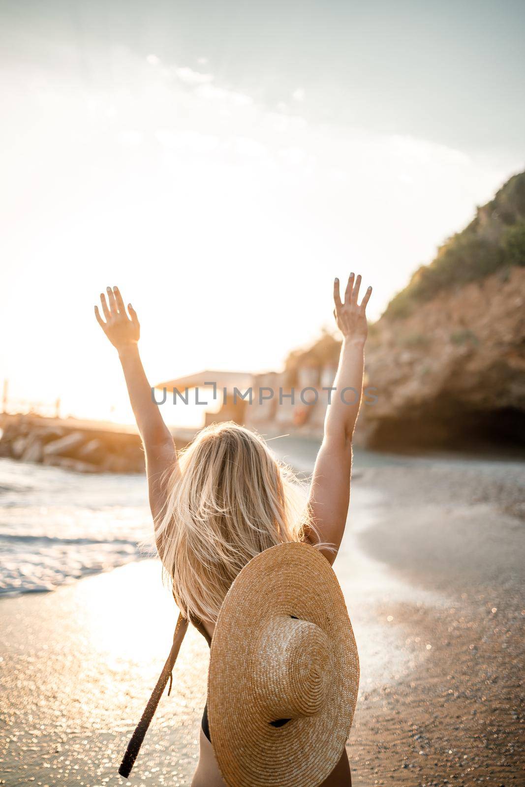 Young beautiful woman in a black swimsuit and hat with glasses walks along the beach in Turkey at sunset. The concept of sea recreation. Selective focus