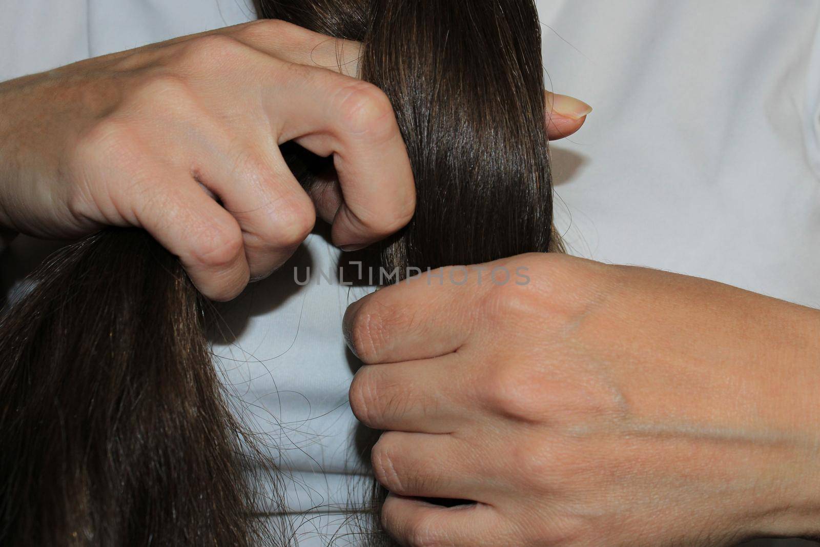 A girl with long dark hair is braiding her hair. Close-up hands. Hair care. Hair loss problem.. by IronG96