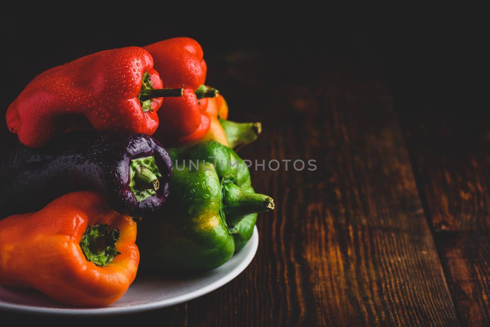 Multicolored fresh bell peppers on plate over wooden background