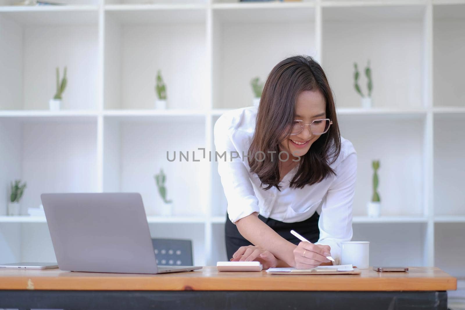 Asian Businesswoman Using laptop computer and working at office with calculator document on desk, doing planning analyzing the financial report, business plan investment, finance analysis concept..