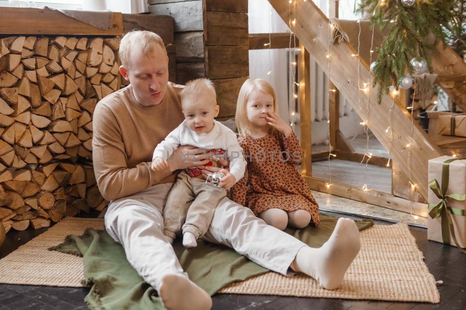 Dad and little brother and sister play on Christmas Eve in a beautiful house decorated for the New Year holidays. The concept of family holidays