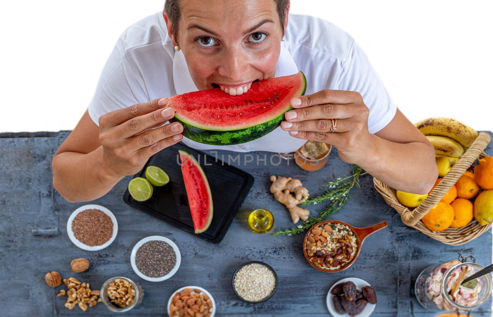 Woman crunching to the teeth watermelon surrounded by cereals, seeds, dried fruits, citrus fruits, ginger and others.