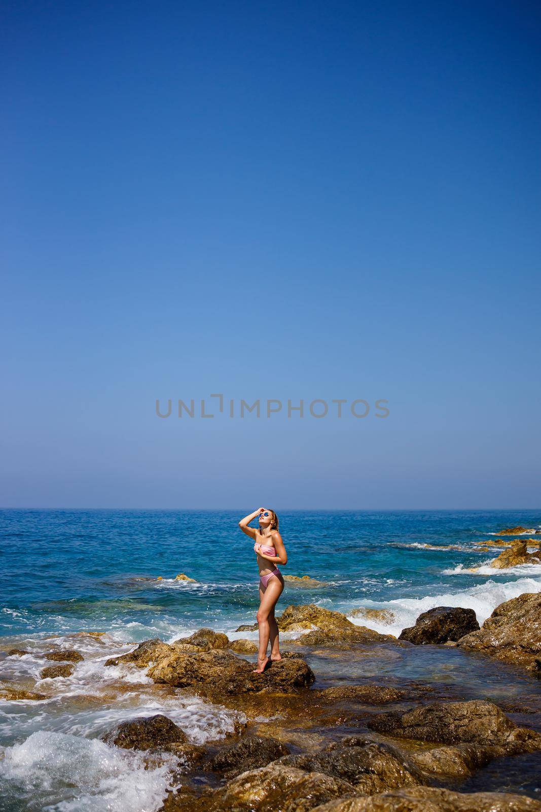 Beautiful young woman in a swimsuit on a rocky beach on a sunny day against the backdrop of waves. Vacation in the summer season. Selective focus