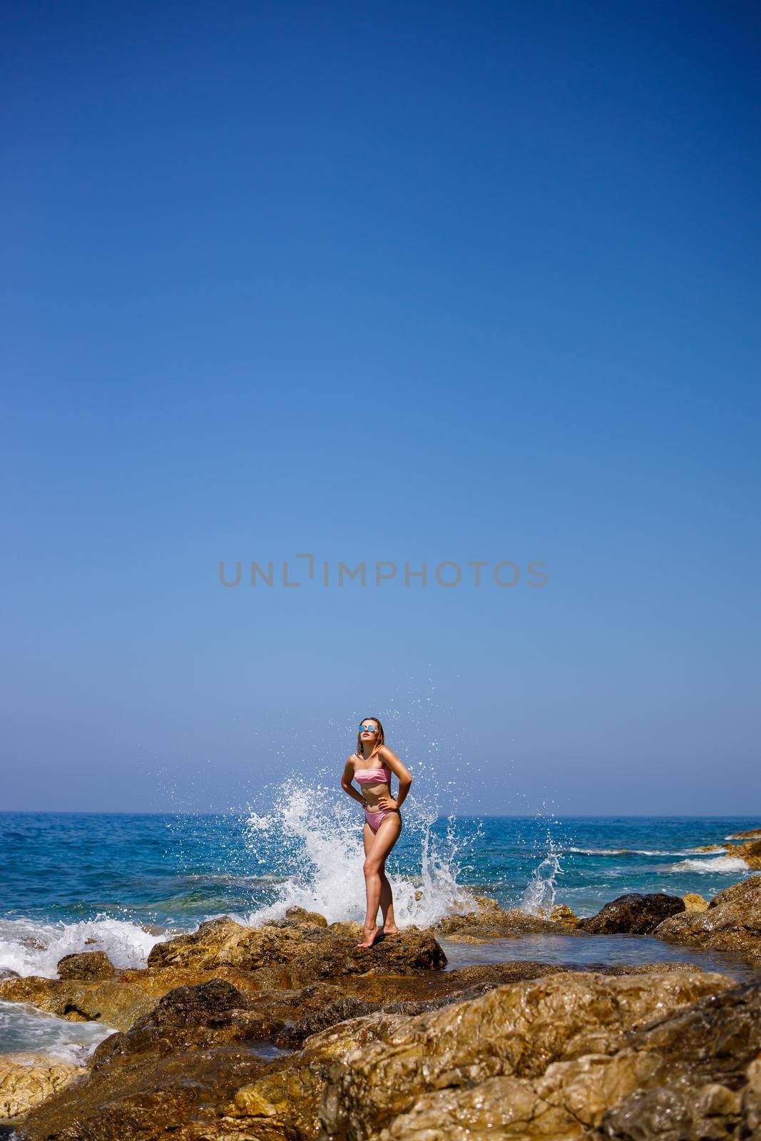 Beautiful young woman in a swimsuit on a rocky beach on a sunny day against the backdrop of waves. Vacation in the summer season. Selective focus