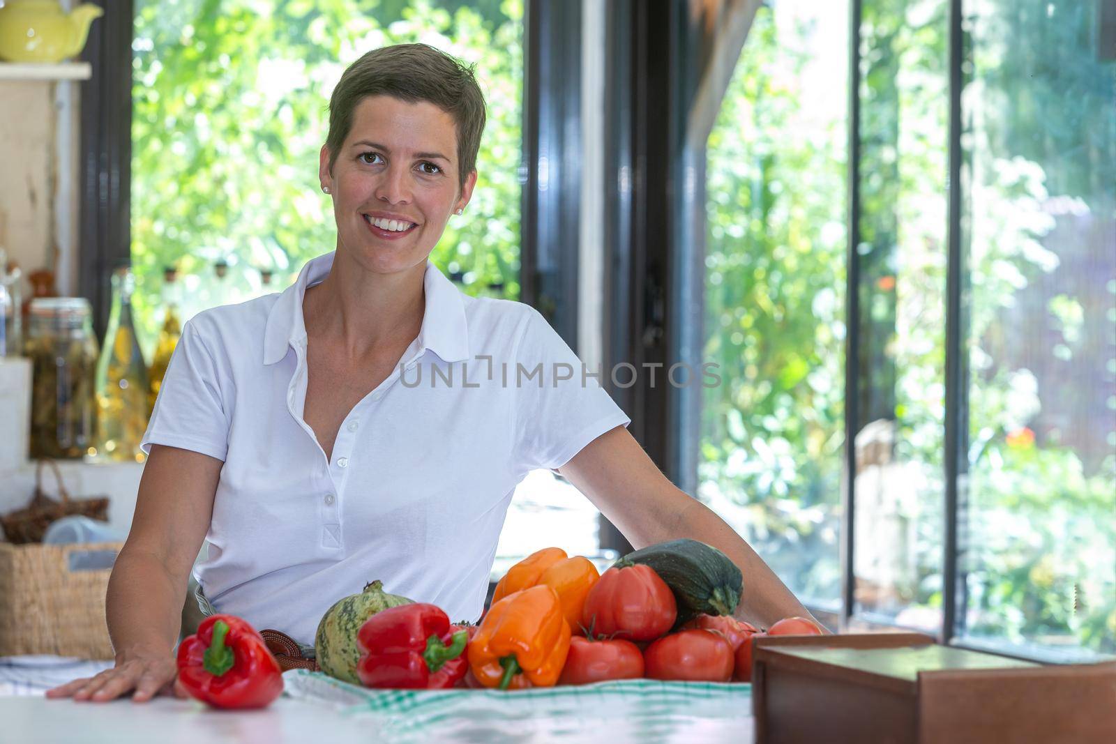 Smiling brown woman with short hair with a bunch of organic vegetables in front of her.