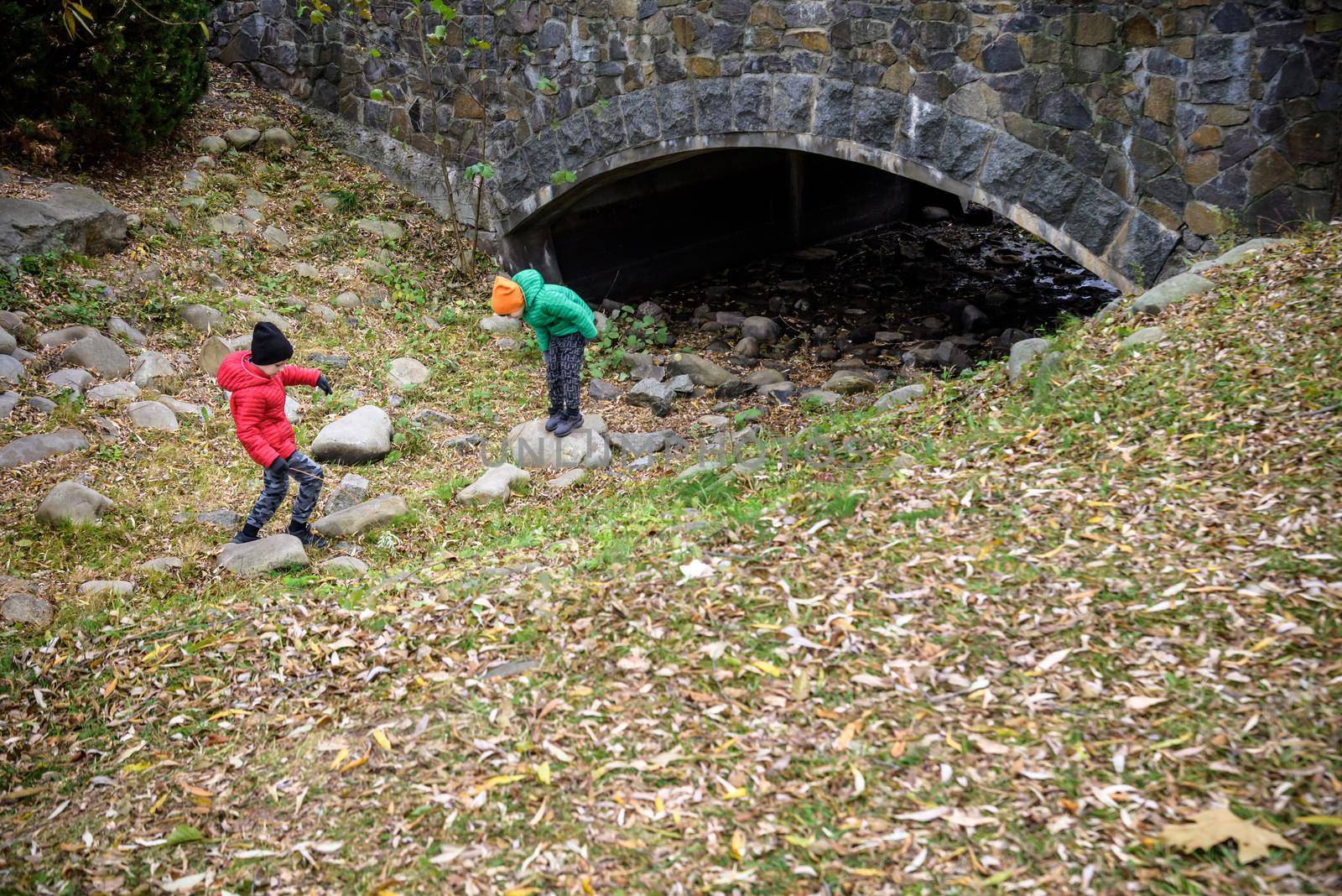Portrait of two boys kid a walk under a brick bridge and looking up, child walking outside, Young boys relaxing outdoors in autumn on bridge. Tourism concept.