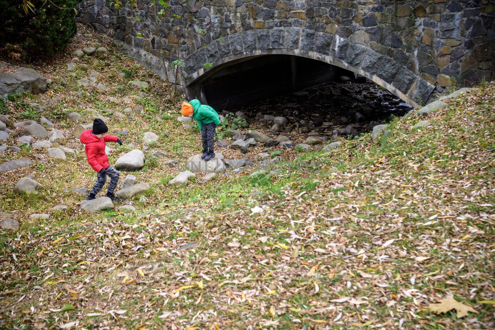 Portrait of two boys kid a walk under a brick bridge and looking up, child walking outside, Young boys relaxing outdoors in autumn on bridge. Tourism concept.