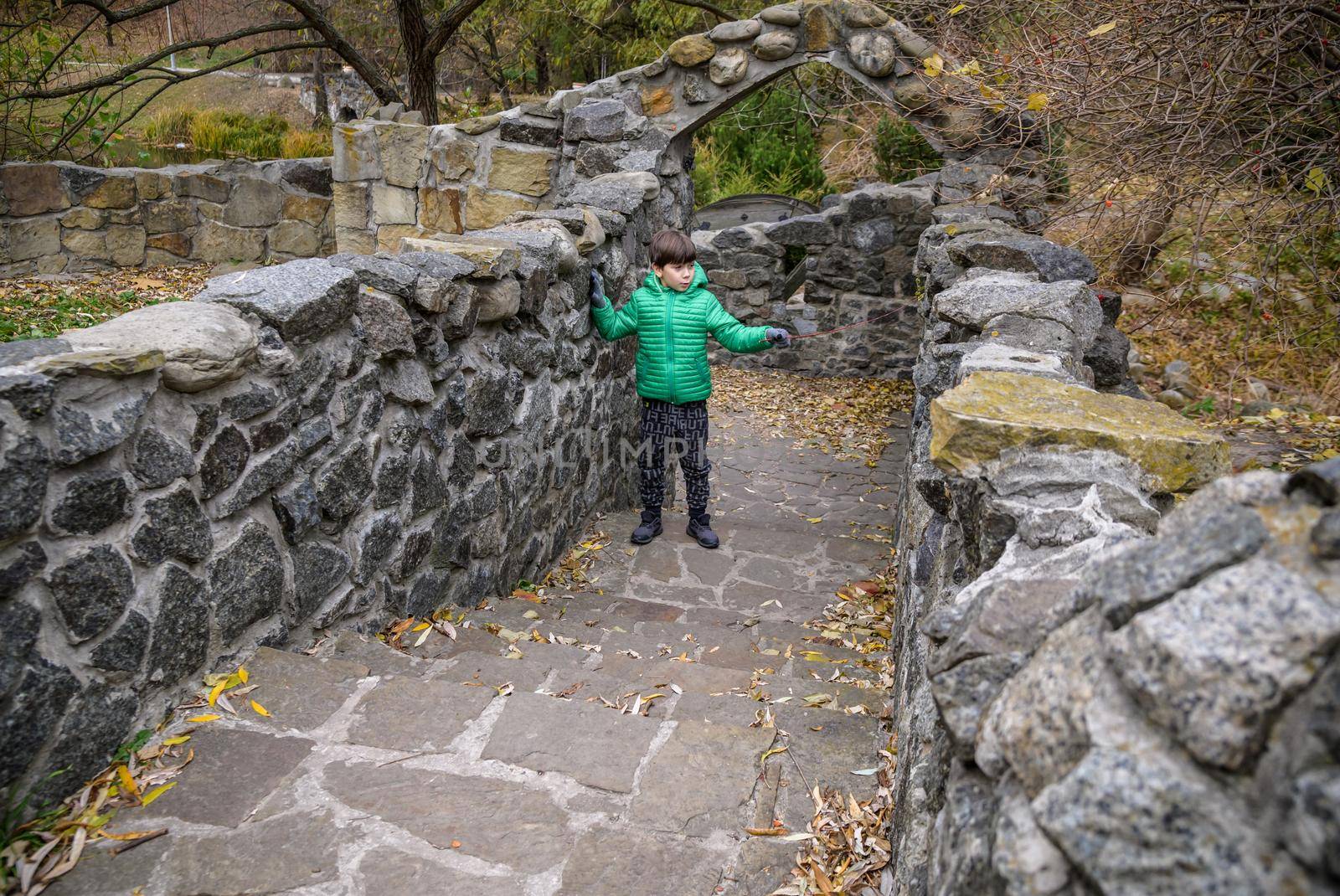 Portrait of boy kid a walk under a brick bridge and looking up, child walking outside, Young boy relaxing outdoors in autumn on bridge. Tourism concept.