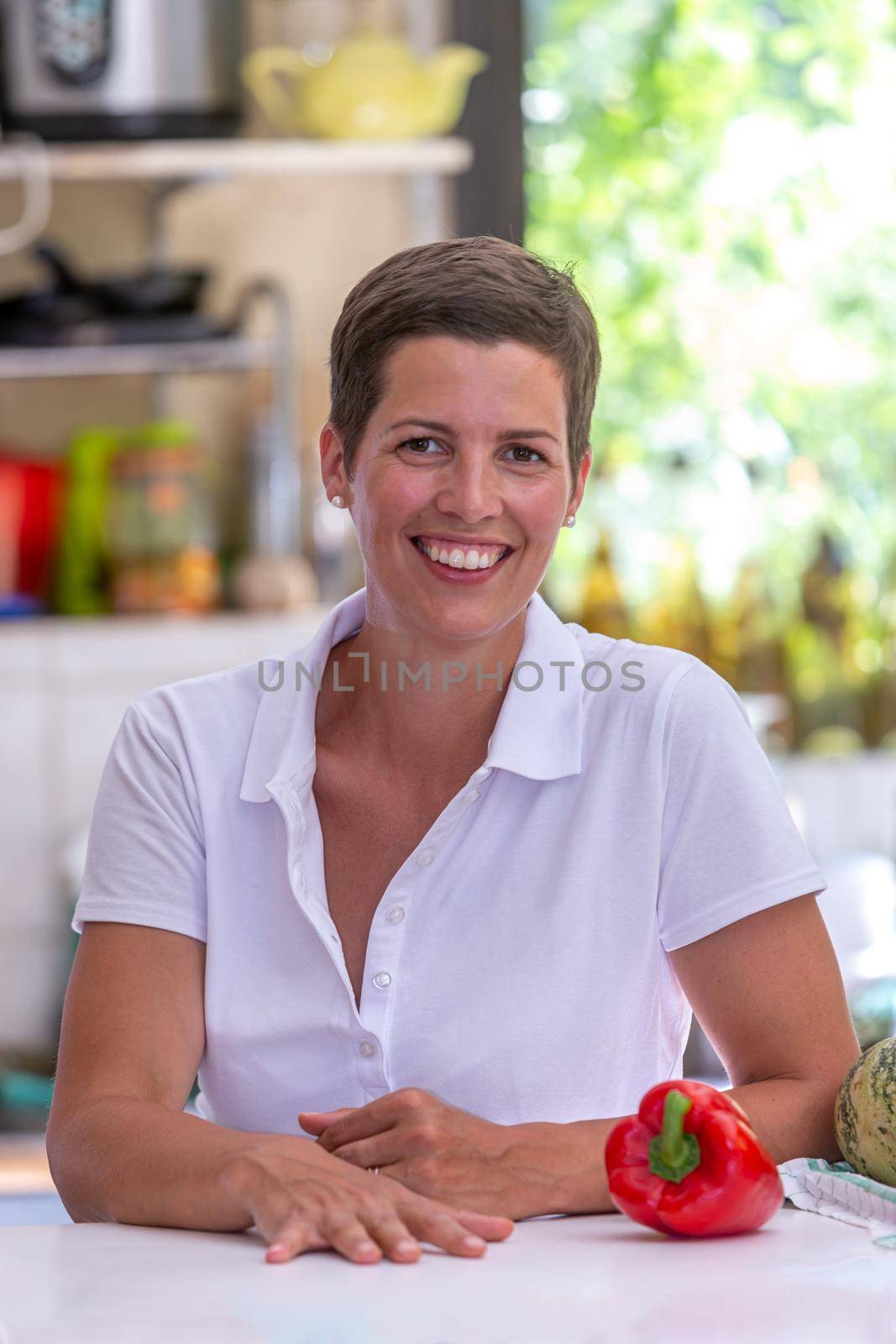 Young brown woman with short hair leaning on a table, kitchen utensils in the background.