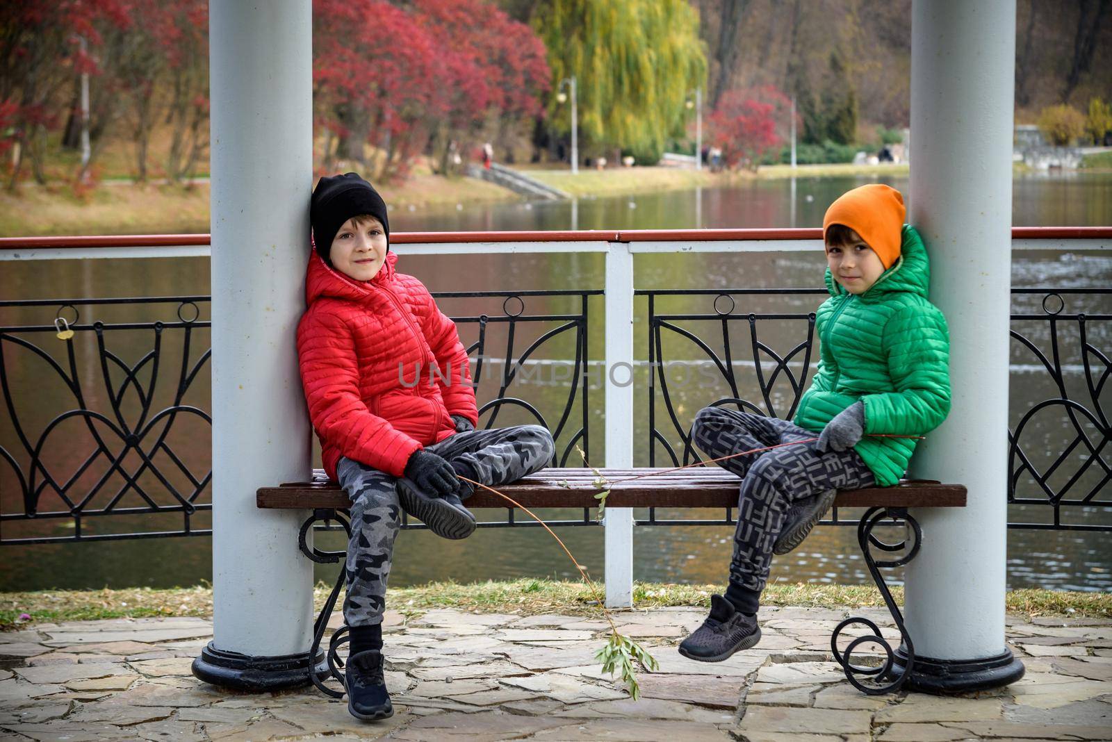 Two siblings stand on the bridge and admire the magnificent view of the autumn forest and its reflection in the lake water. Autumn walk. Outdoor lifestyle, active family lifestyle.