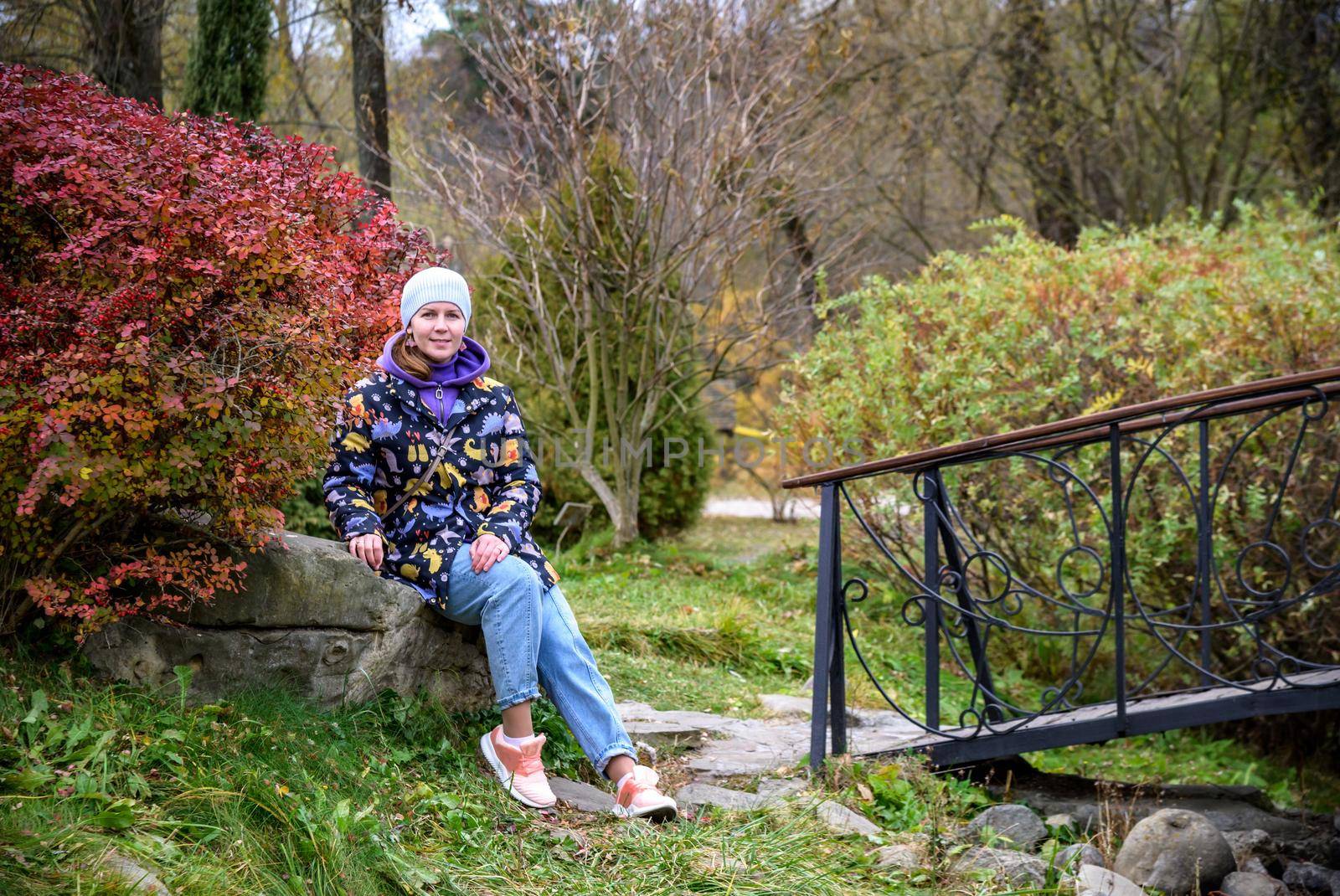 Carefree young woman in trendy vintage pants sitting on table in park and laughing. Curly cute girl in good mood posing in autumn day, enjoying good weather.