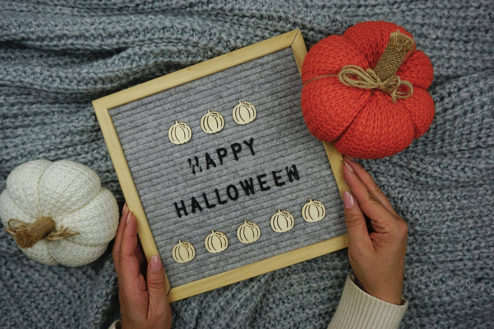 On a knitted gray background, a sign with the inscription - happy Halloween and there are knitted pumpkins by Spirina
