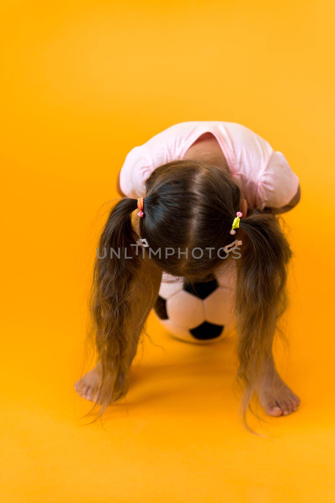 Authentic cute smiling preschool little girl with classic black and white soccer ball look at camera on yellow background. child play football in t-shirt and shorts. Sport, championship, team concept.