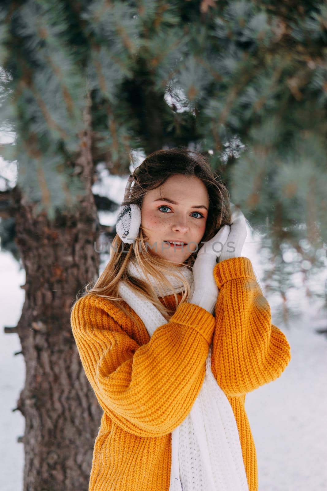 Teen blonde in a yellow sweater outside in winter. A teenage girl on a walk in winter clothes in a snowy forest.