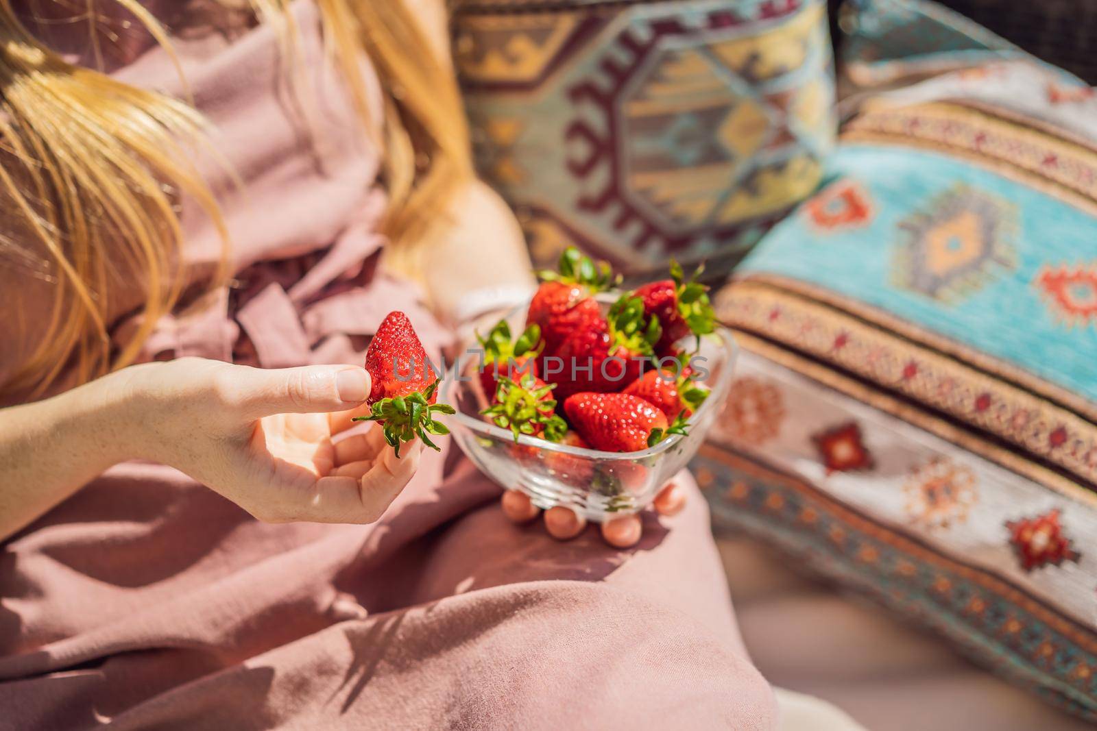 Portrait of gorgeous woman wearing beautiful dress sitting in a patio and eating strawberry.