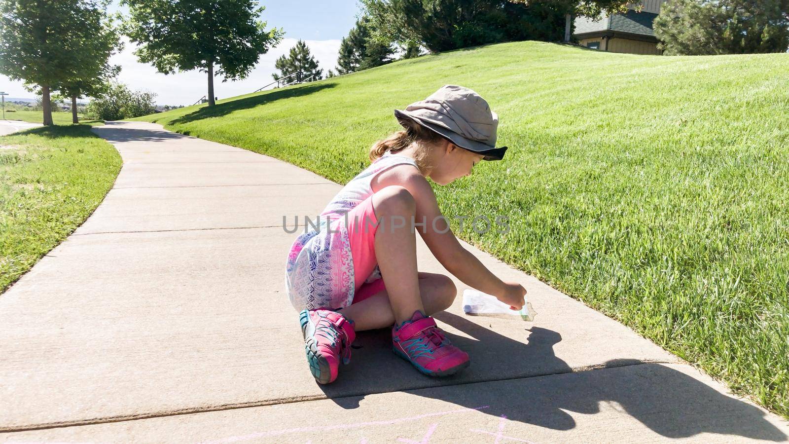 Little girl drawing with chalk on a sidewalk on the summer day.