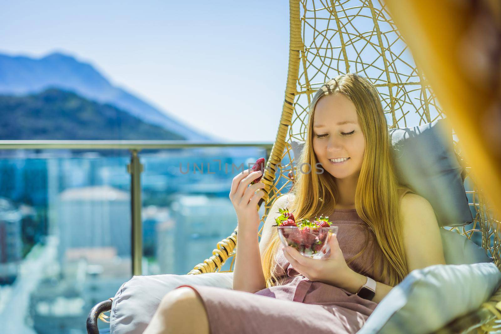 Portrait of gorgeous woman wearing beautiful dress sitting in a patio and eating strawberry.