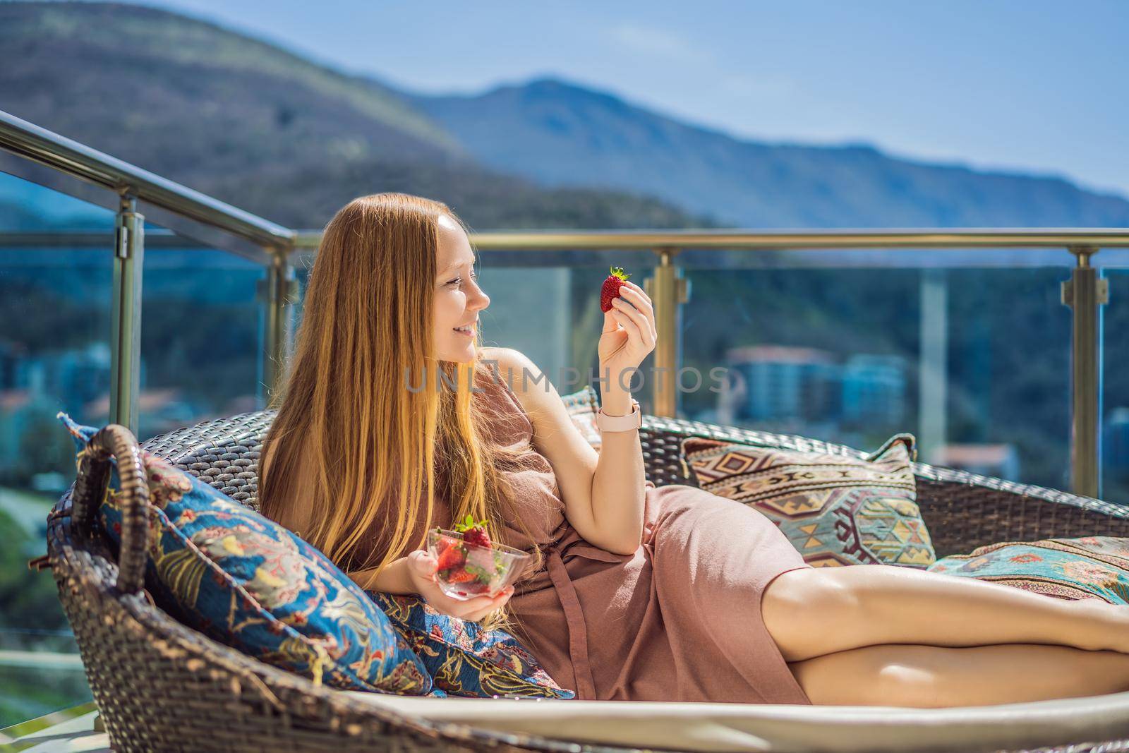 Portrait of gorgeous woman wearing beautiful dress sitting in a patio and eating strawberry.