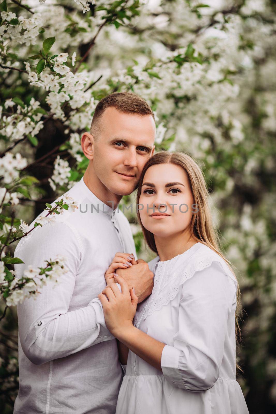 Happy family couple in love in a spring blooming apple orchard. Happy family enjoy each other while walking in the garden. The man holds the woman's hand. Family relationships