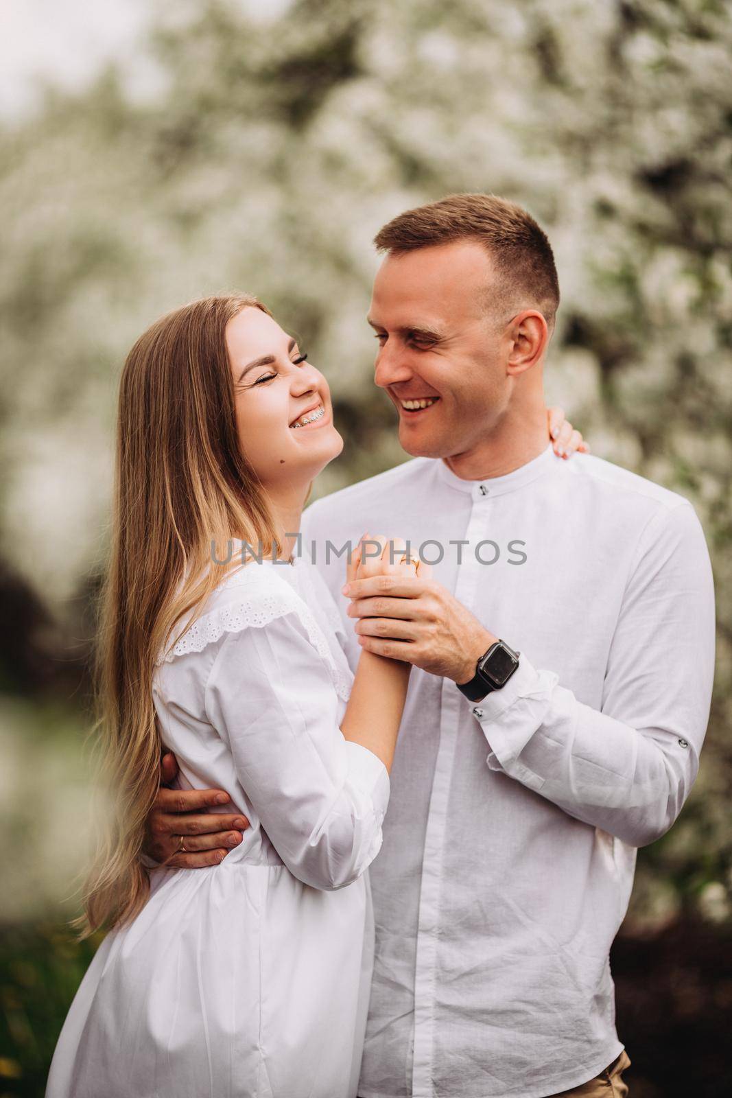 Young loving couple in a walk in a spring blooming apple orchard. Happy married couple enjoy each other while walking in the garden. Man holding woman's hand by Dmitrytph