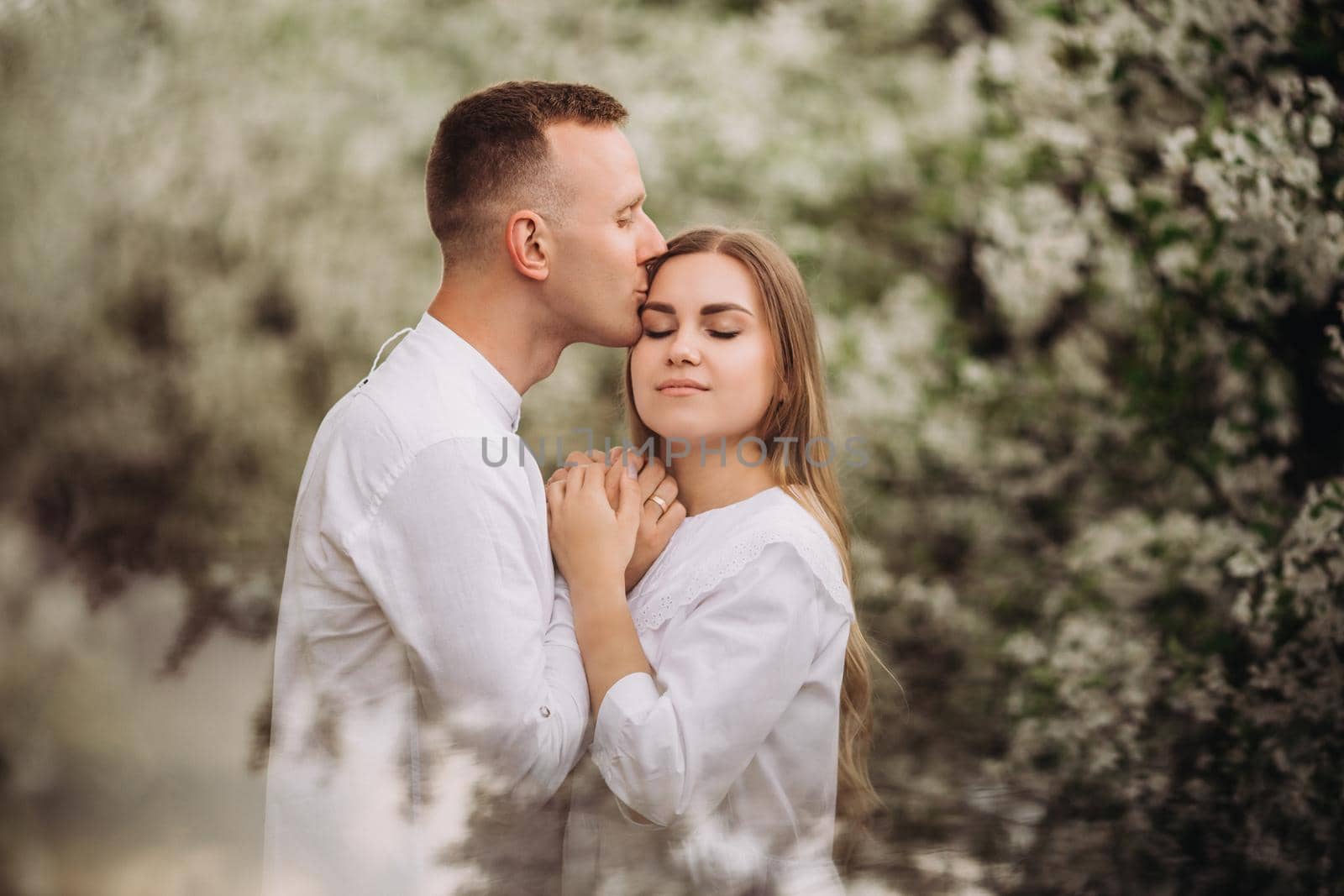 Happy family couple in love in a spring blooming apple orchard. Happy family enjoy each other while walking in the garden. The man holds the woman's hand. Family relationships by Dmitrytph