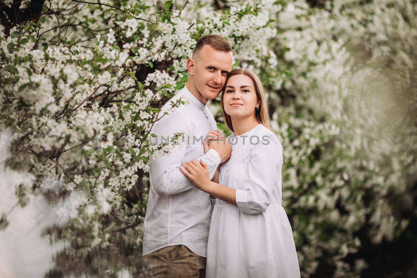 Happy family couple in love in a spring blooming apple orchard. Happy family enjoy each other while walking in the garden. The man holds the woman's hand. Family relationships