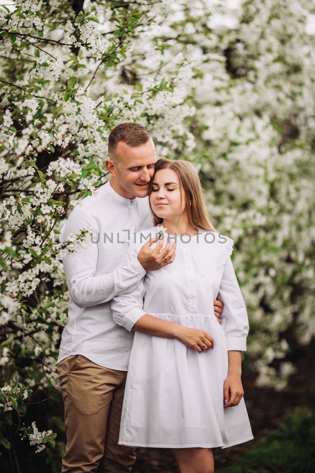 Happy family couple in love in a spring blooming apple orchard. Happy family enjoy each other while walking in the garden. The man holds the woman's hand. Family relationships by Dmitrytph