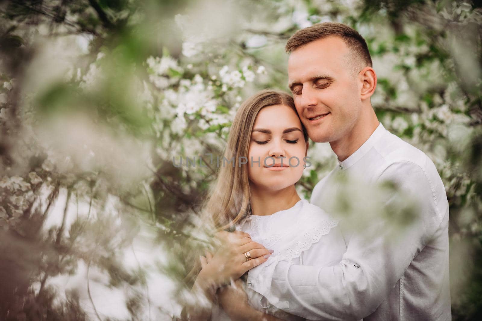 Happy family couple in love in a spring blooming apple orchard. Happy family enjoy each other while walking in the garden. The man holds the woman's hand. Family relationships