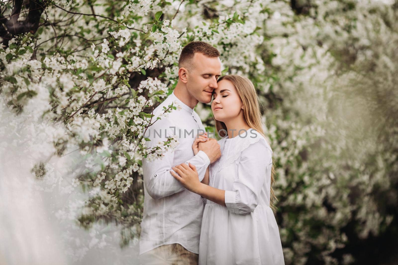 Happy family couple in love in a spring blooming apple orchard. Happy family enjoy each other while walking in the garden. The man holds the woman's hand. Family relationships