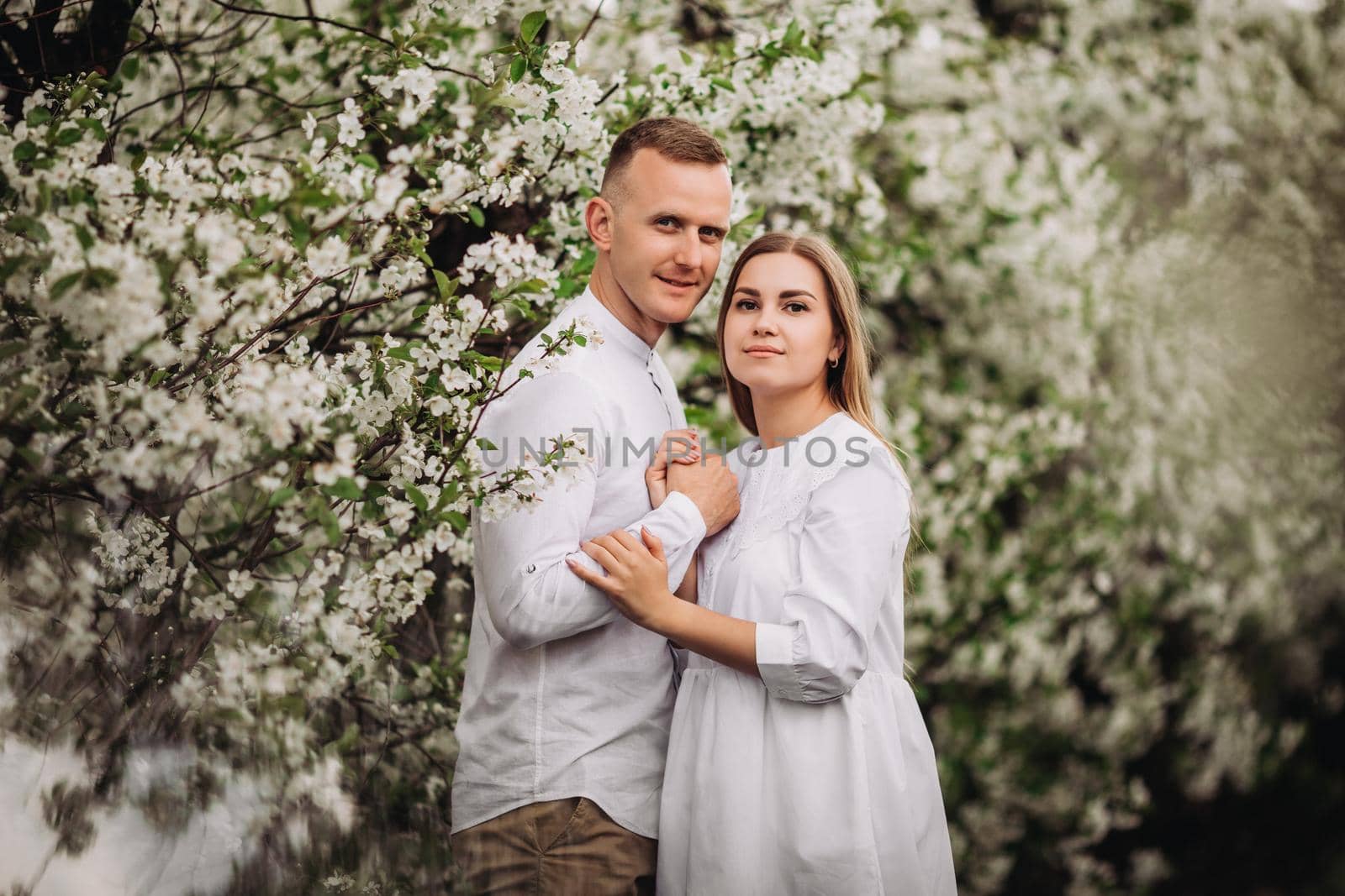 Happy family couple in love in a spring blooming apple orchard. Happy family enjoy each other while walking in the garden. The man holds the woman's hand. Family relationships by Dmitrytph