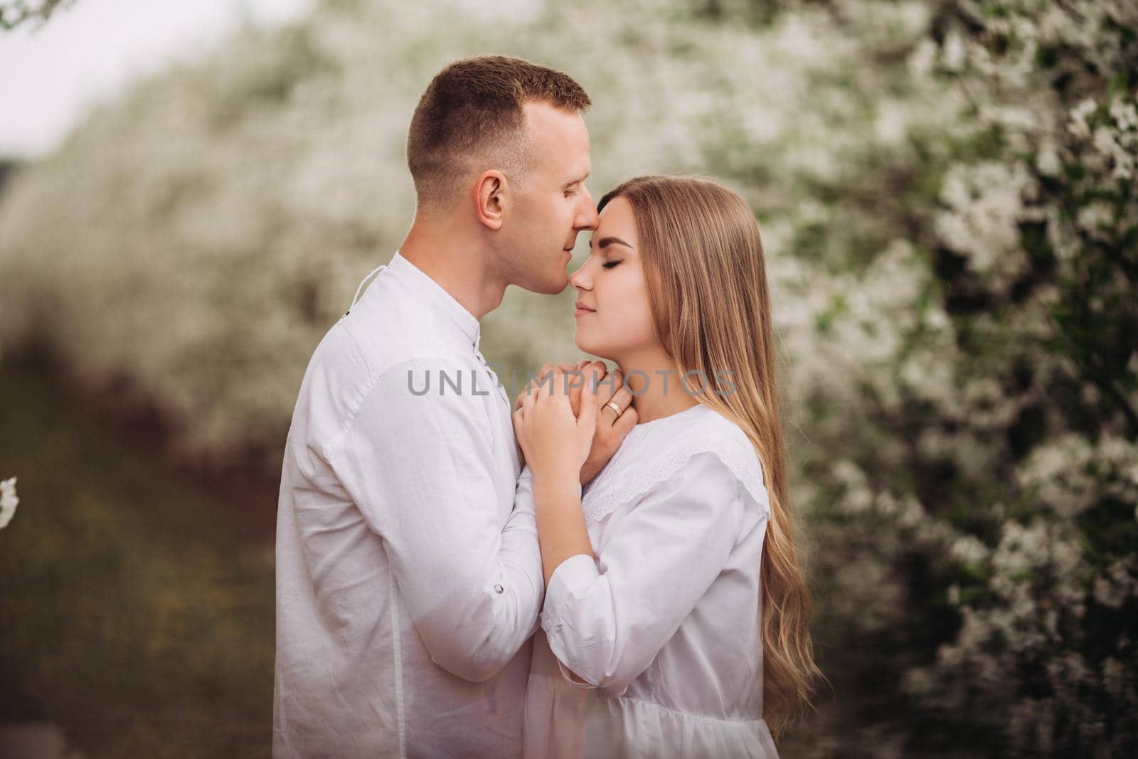 Young loving couple in a walk in a spring blooming apple orchard. Happy married couple enjoy each other while walking in the garden. Man holding woman's hand